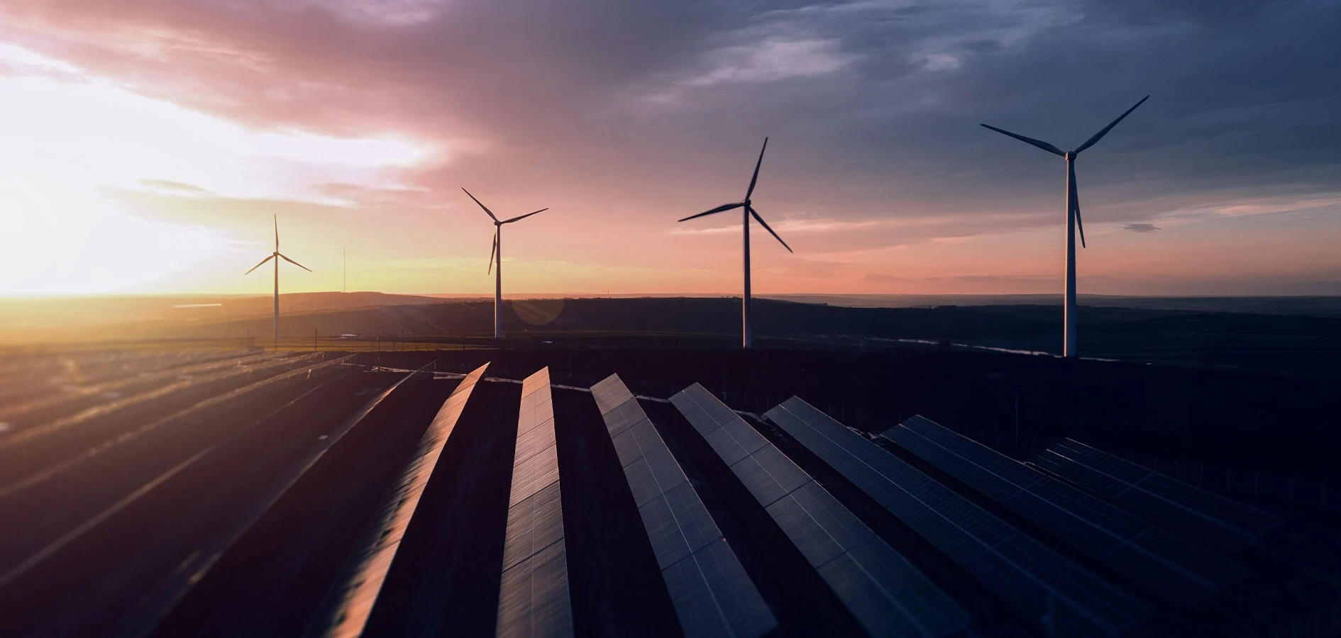 Wind turbines and solar panels across an energy landscape at sunset.